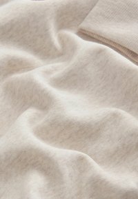 Blødt, lyst beige stof med en glat tekstur og subtile farvevariationer, der har en let ribbet sektion i øverste højre hjørne.