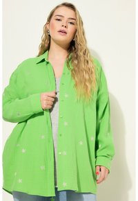 Zelená košile na knoflíky vyrobená z texturované látky, s motivy stříbrných hvězd. Nositá přes šedý top s volným střihem a dlouhými rukávy.