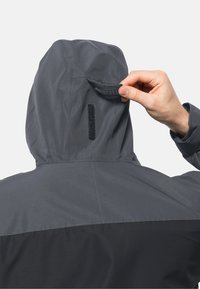 Grijze hooded jas met een zwarte onderkant. Bevat een klittenbandsluiting bij de nek en een zwart stoffen accent langs de naad.