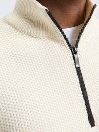 Cream, textured knit pullover with a high collar and black zipper. Features a contrasting zipper pull, close-fitting design, and ribbed edges.