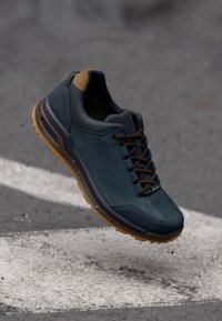 Blå og grå atletiske sko med gummisåle, teksturert overdel og brune detaljer. Har polstret krage og kontrasterende snører.