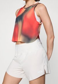 Débardeur rouge et dégradé avec des accents noirs, associé à un short blanc doté d'un logo brodé et de fentes latérales pour la mobilité.