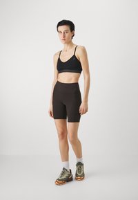 Schwarzer Sport-BH und hochgeschnittene braune Shorts kombiniert mit grünen und orangefarbenen Sportschuhen, die eine strukturierte Oberfläche und eine schlanke Passform bieten.