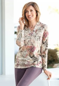 Blumenbluse mit langen Ärmeln aus leichtem Stoff in Rosa- und Lilatönen; kombiniert mit lila Hosen. V-Ausschnitt-Design und dezente Texturdetails.