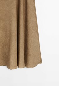 Jupe trapèze beige avec une texture de tissu douce, tombant naturellement sur un fond blanc.
