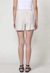 Short beige clair en lin avec une finition texturée. Comprend une taille élastique et un bord festonné noir le long de l'ourlet.