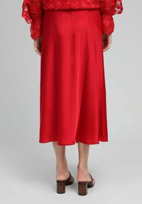 Jupe midi en satin rouge avec une texture lisse, une forme évasée et une fente sur le côté, associée à des sandales à talons marron.