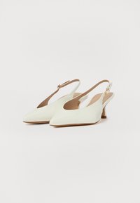 Tacones slingback de charol blanco con punta afilada, un tacón delgado y un forro interior beige; cuenta con una correa con un cierre dorado.
