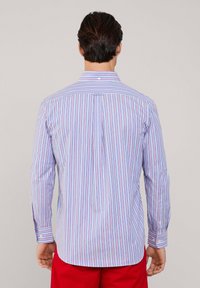 Camisa a rayas que presenta colores azul claro, rosa y blanco, con cuello extendido, mangas largas y puños abotonados. Detalle de pliegue en la parte posterior.