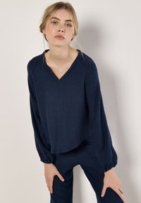 Navyblaues, strukturiertes Strickoberteil mit V-Ausschnitt, überschnittenen Schultern und langen Ärmeln. Kombiniert mit passenden Hosen für einen abgestimmten Look.