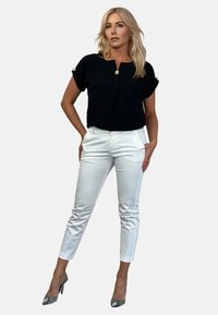 Czarny krótki top z okrągłym dekoltem i detalem w postaci guzików, połączony z dopasowanymi białymi spodniami oraz teksturowanymi szpilkami w wężowy wzór.