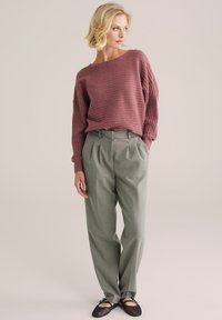 Burgundy bordázott kötött pulóver széles, boát nyakú kivágással, világosszürke pliszírozott nadrág és fekete hálós balerina cipők. Semleges háttér.