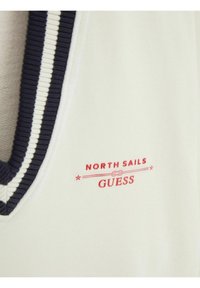 Tissu crème avec col côtelé rayé bleu marine et blanc, présentant des logos texte rouges "North Sails" et "Guess" sur la poitrine.