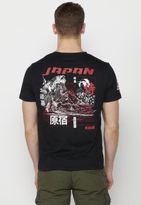 Fekete póló, amelyen grafikai ábrázolás található a Fujisan-hegyről, szamurájról és japán feliratról piros és fehér színben, bemutatva egy merész, modern esztétikát.