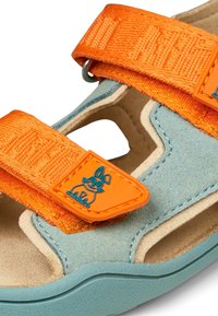 Sandalini per bambini con cinghie regolabili arancioni, base in suede azzurro chiaro, soletta beige e un'etichetta arancione con un design di un coniglietto cartone.