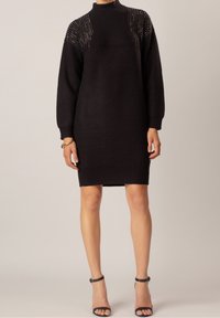 Robe tricotée noire avec un col haut et des manches trois-quarts. Présente des accents ornés de bijoux sur les épaules et une silhouette ajustée.