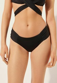 Černé bikiny s řaseným designem po stranách, vyrobené z elastického materiálu, který zajišťuje těsné padnutí.