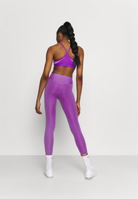 Reggiseno sportivo viola con design a incrocio sul retro, abbinato a leggings viola a vita alta. Tessuto morbido, vestibilità atletica, dettagli di cucitura minimi.