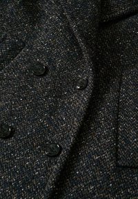 Tissu de manteau en laine texturée gris foncé montrant quatre boutons noirs brillants disposés en double boutonnage.