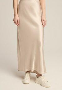 Beżowa satynowa spódnica maxi o gładkiej fakturze, w połączeniu z białymi sneakersami z wiązaniem. Spódnica sięga kostek, tworząc płynną sylwetkę.