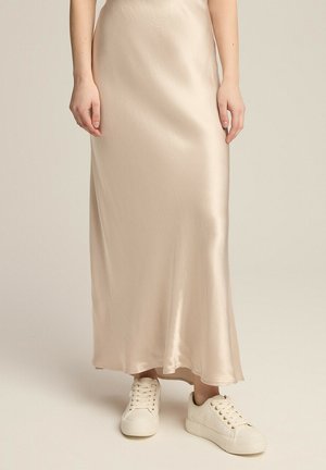 Beżowa satynowa spódnica maxi o gładkiej fakturze, w połączeniu z białymi sneakersami z wiązaniem. Spódnica sięga kostek, tworząc płynną sylwetkę.