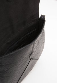 Svart läderhandväska med texturerad yta. Insidan har ett blixtlåsförsett ficka, mjukt tygfoder och stängning med övre klaff.