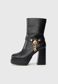 Fekete bőr platform bokacsizma, tömbsarkal, arany lánccal és díszes medál részlettel az oldalon.