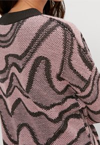 Pull en tricot rose avec des motifs ondulés noirs, présentant un tissage texturé et un col noir contrastant.