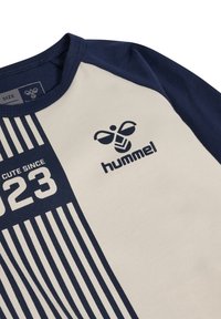 Korte mouwen Hummel-shirt met een crèmekleurig lijf en marineblauwe mouwen. Met verticale marineblauwe strepen, merklogo en de tekst "CUTE SINCE 2023".
