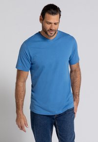 Royalblauwe T-shirt met korte mouwen en V-hals, gemaakt van zachte stof, gecombineerd met blauwe jeans. De pasvorm is ontspannen, wat het casual ontwerp benadrukt.