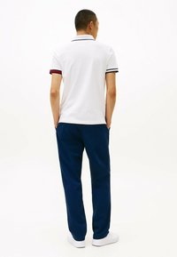 Witte polo met gekleurde strepen op de manchetten, gecombineerd met blauwe broek. De outfit heeft een eenvoudig, strak ontwerp en een relaxte pasvorm.