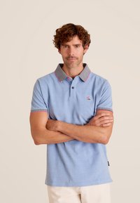 Lichtblauw poloshirt met een gestreepte kraag in zwart en wit, accentueert met roze biezen, heeft korte mouwen en een klein patchlogo.