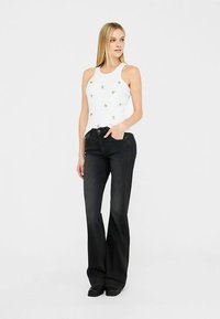 Valge tanktop väikeste kaunistustega, kombineeritud mustade lehvikpükstega. Taust on lihtne, rõhutades rõivastuse detaile.