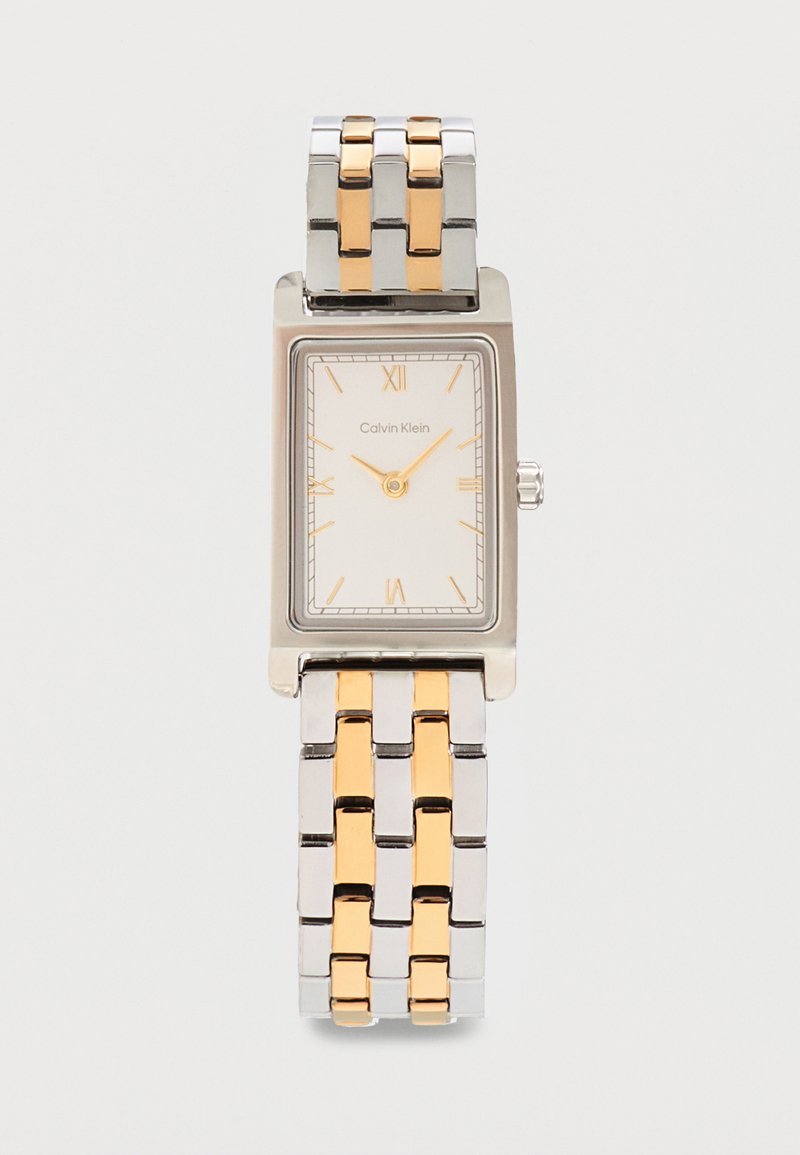 Montre-bracelet rectangulaire Calvin Klein en argent et or avec cadran blanc, chiffres romains dorés et bracelet métallique bicolore.