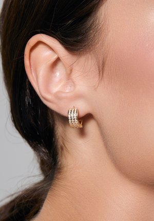 Złote kolczyki w formie obręczy z trzema rzędami małych, przezroczystych kryształków. Projekt jest gładki, z polerowanym wykończeniem i okrągłym kształtem.