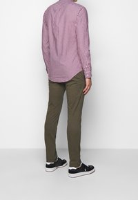 Red and white checked long-sleeve shirt, green slim-fit pants, and black sneakers with white accents, viewed from the back.