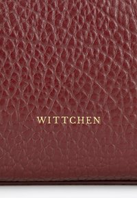 Bordowa skórzana torebka o teksturowanej powierzchni. Posiada wyraźnie umieszczone złote logo "Wittchen". Kompaktowy, prostokątny kształt.
