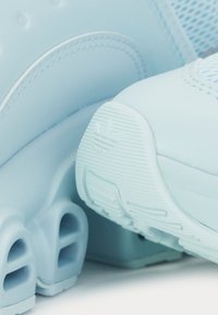 Hele sinine spordijALan, millel on sile ülemine osa ja võrkmaterjali detailid, tekstuuriga tald ja kaubamärgi aktsent kandade peal.