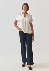 White short-sleeve blouse with a V-neck and button detail, paired with navy wide-leg jeans and black ballet flats. Smooth fabric texture.