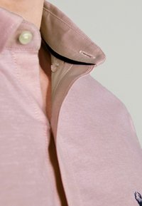 Lichtroze polo-shirt met een knoopje-kraag, voorzien van een contrasterende zwarte binnenkant en subtiele textuur, met een klein geborduurd logo.