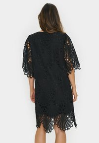Black lace dress featuring a detailed pattern with scalloped edges and wide sleeves, showcasing intricate cut-out designs and a loose fit.