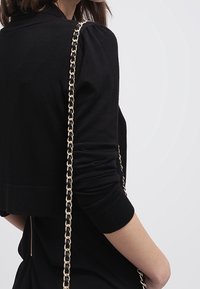 Suéter negro corto con mangas abullonadas, combinado con un bolso de cadena dorada. Textura suave con un diseño minimalista.