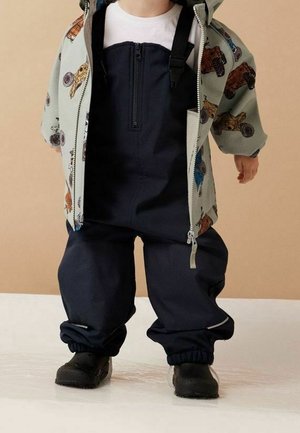 Ensemble pour enfant comprenant une veste zippée vert clair avec des imprimés de véhicules colorés et des salopettes imperméables navy à bretelles réglables, chaussures noires.
