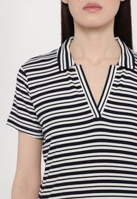 Triibuline polo särk tumesinises ja valges, soonikstruktuuriga, kaelusega ja V-kujulise lõikega. Lühikesed varrukad kontrastset triibu aktsentidega.