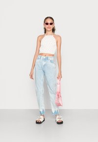 Top crop branco com padrão floral, jeans de cintura alta azul claro, sandálias pretas com tiras brancas e uma bolsa transparente rosa.