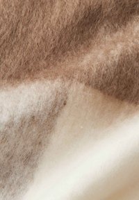 Tessuto di lana in tonalità di marrone e crema, che mostra una consistenza morbida con una miscela di motivi, comprese aree chiare e scure.