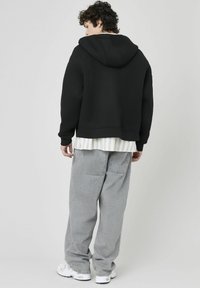 Haut de hoodie noir coupé avec une texture douce, superposé sur une chemise rayée blanche. Porté avec un pantalon gris à coupe décontractée et des baskets blanches.