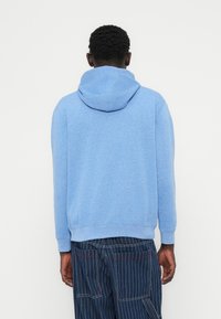 Μπλε φούτερ με κουκούλα από απαλό υλικό, με κορδόνι στην κουκούλα, ριμπ μανσέτες και άνετη εφαρμογή, εμφανίζεται από πίσω.