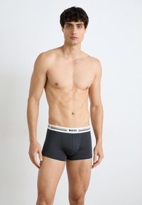 Schwarze Boxer-Brief mit weißem elastischem Bund, der das "BOSS"-Logo und doppelte schwarze Streifen zeigt. Weicher Stoff mit enganliegendem Design.