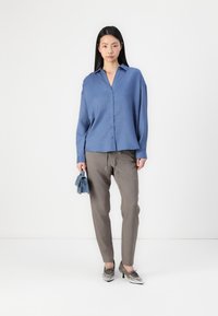 Light blue oversized button-up shirt, gray tailored trousers, silver shoes, holding a folded blue cloth. Minimalist design, smooth texture.